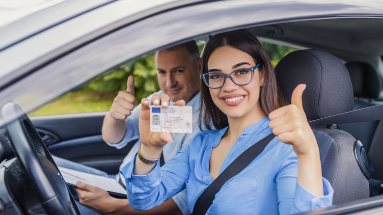 A woman holding up a drivers license after passing the practical test